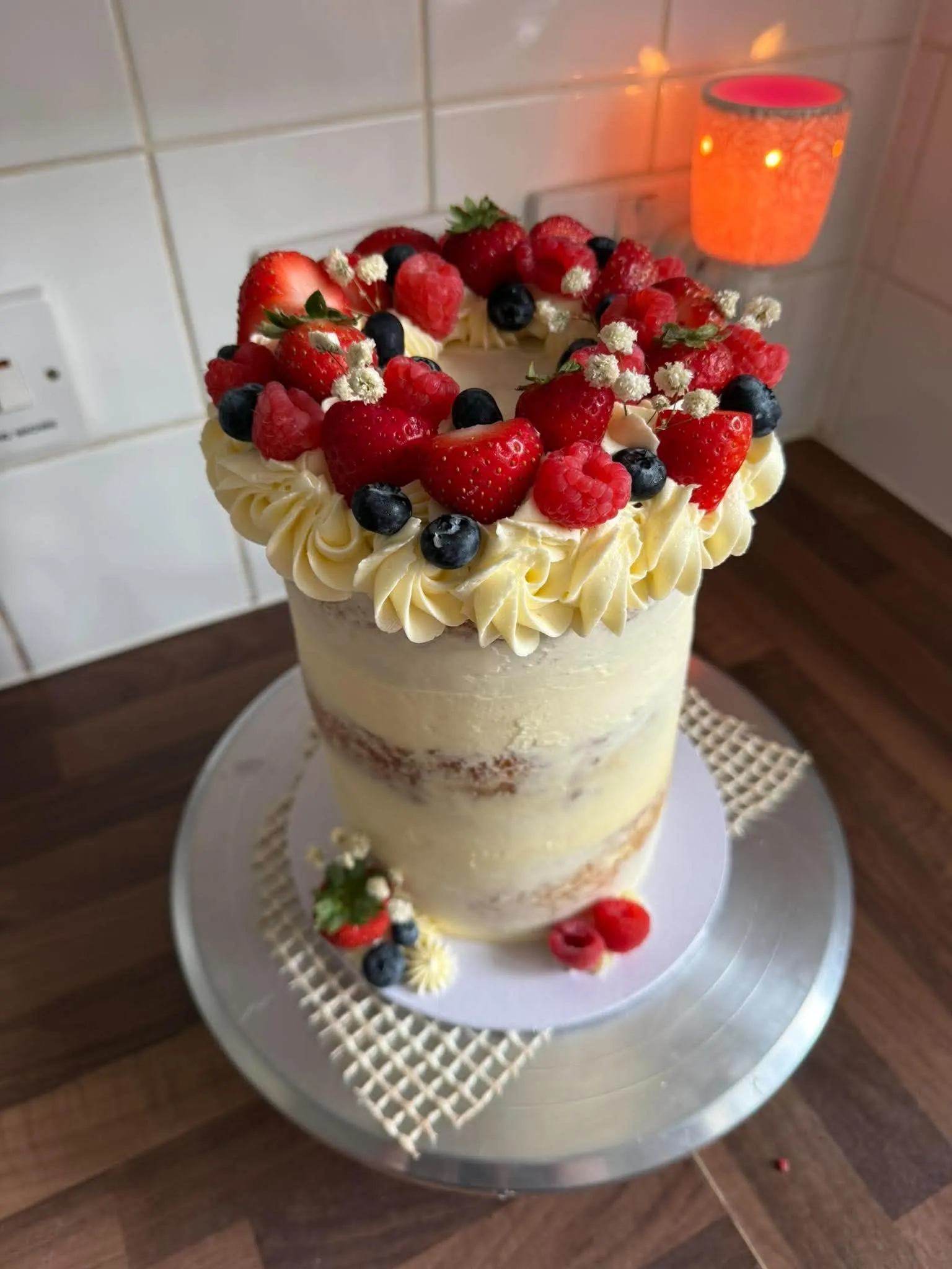 A tall vanilla cake with cream piped round the top and piled with strawberries, raspberries and blueberries