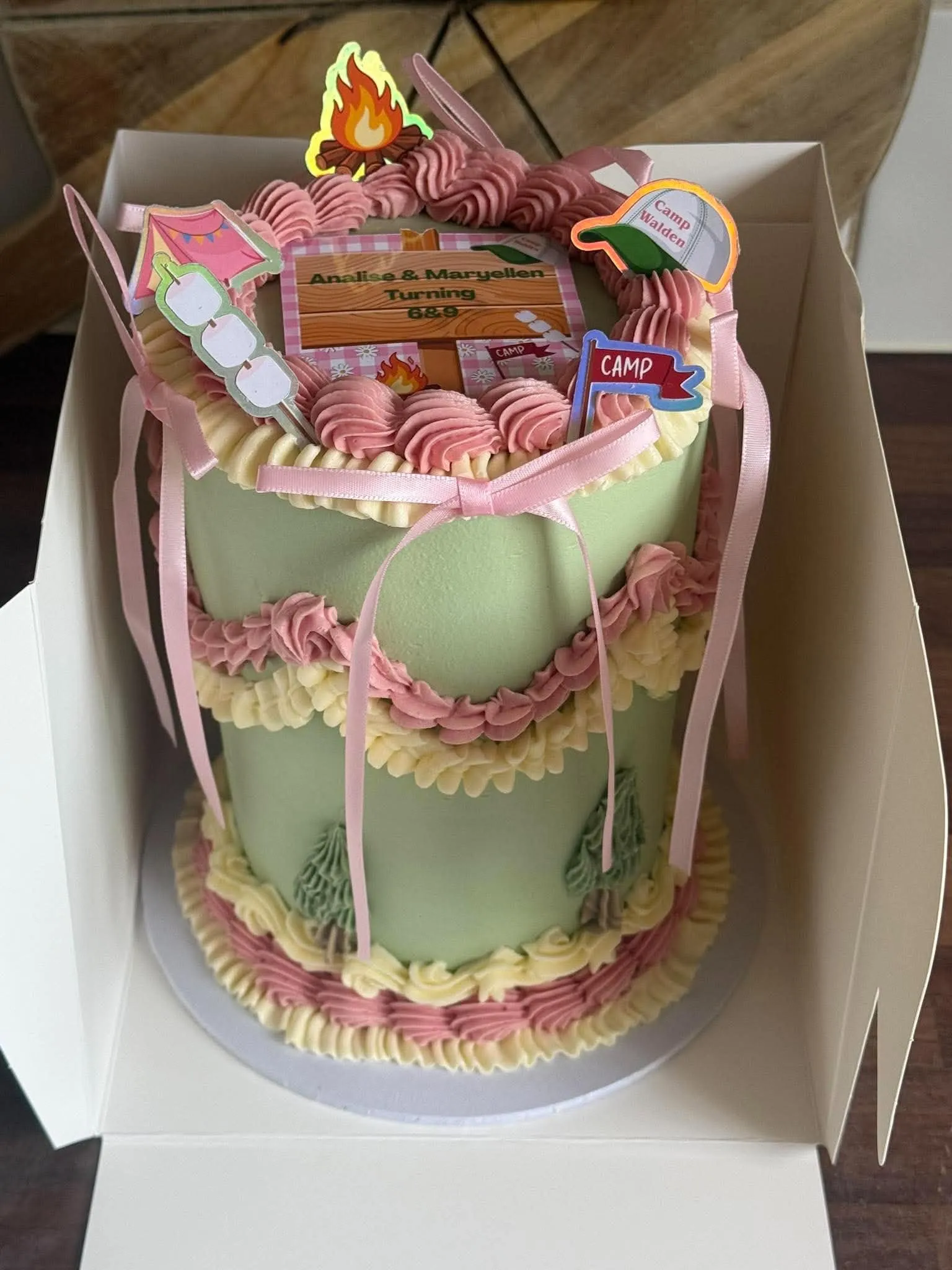 Cake 3: A pale green cake with piped pink and cream bows and a camping theme