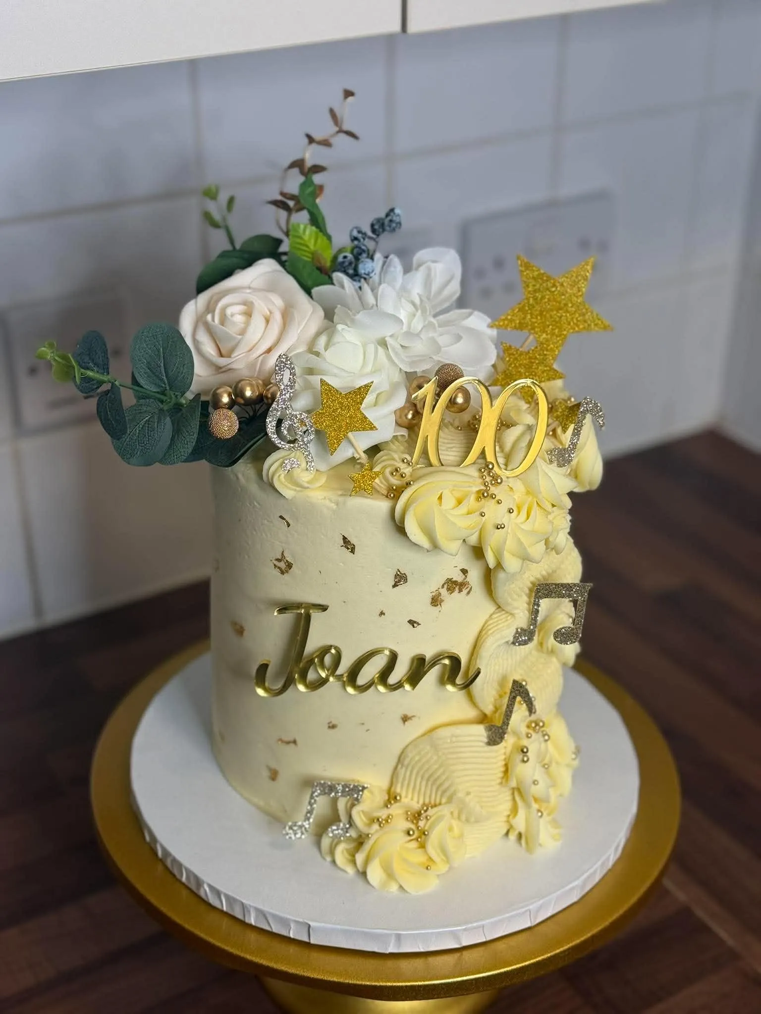A gold and cream cake with roses and stars for a 100th birthday