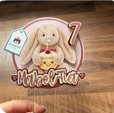 A layered round cake topper with a bunny holding a cupcake, a pink number seven and a name