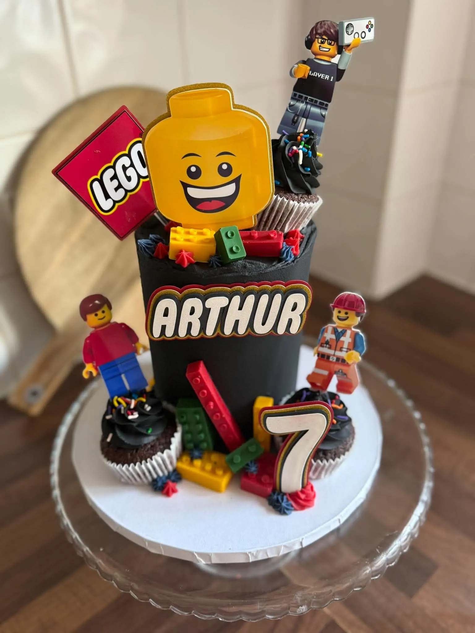 Cake 10: A black cake with a big yellow brick-figure head, a name and chocolate cupcakes