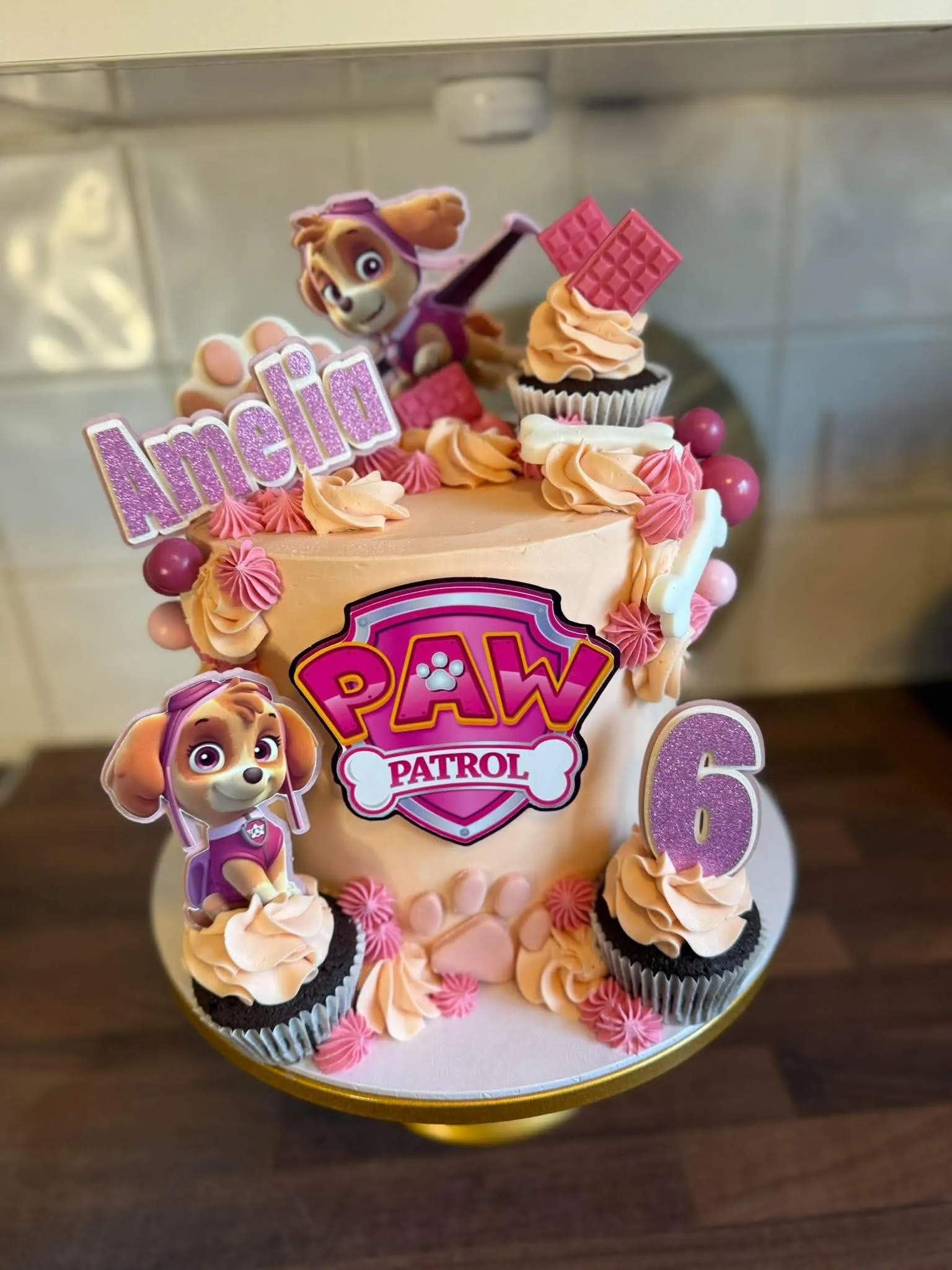 Cake 7: A pale pink cake with cupcakes, a name and a number six, decorated with a puppy-patrol theme
