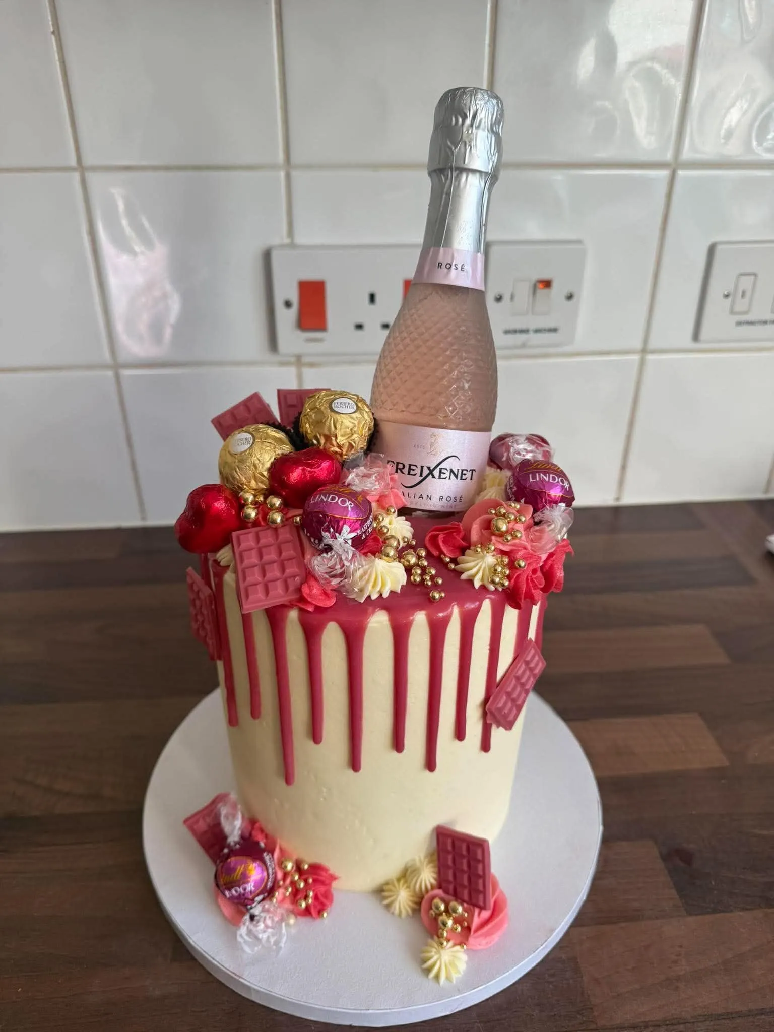 Cake 4: A tall cake with a pink drip, chocolates and a bottle of sparkling wine on top