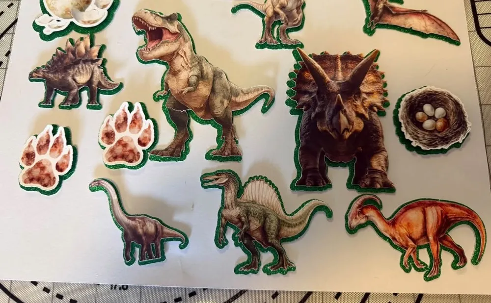 A sheet of hand-cut dinosaur cake toppers with glittery green edges
